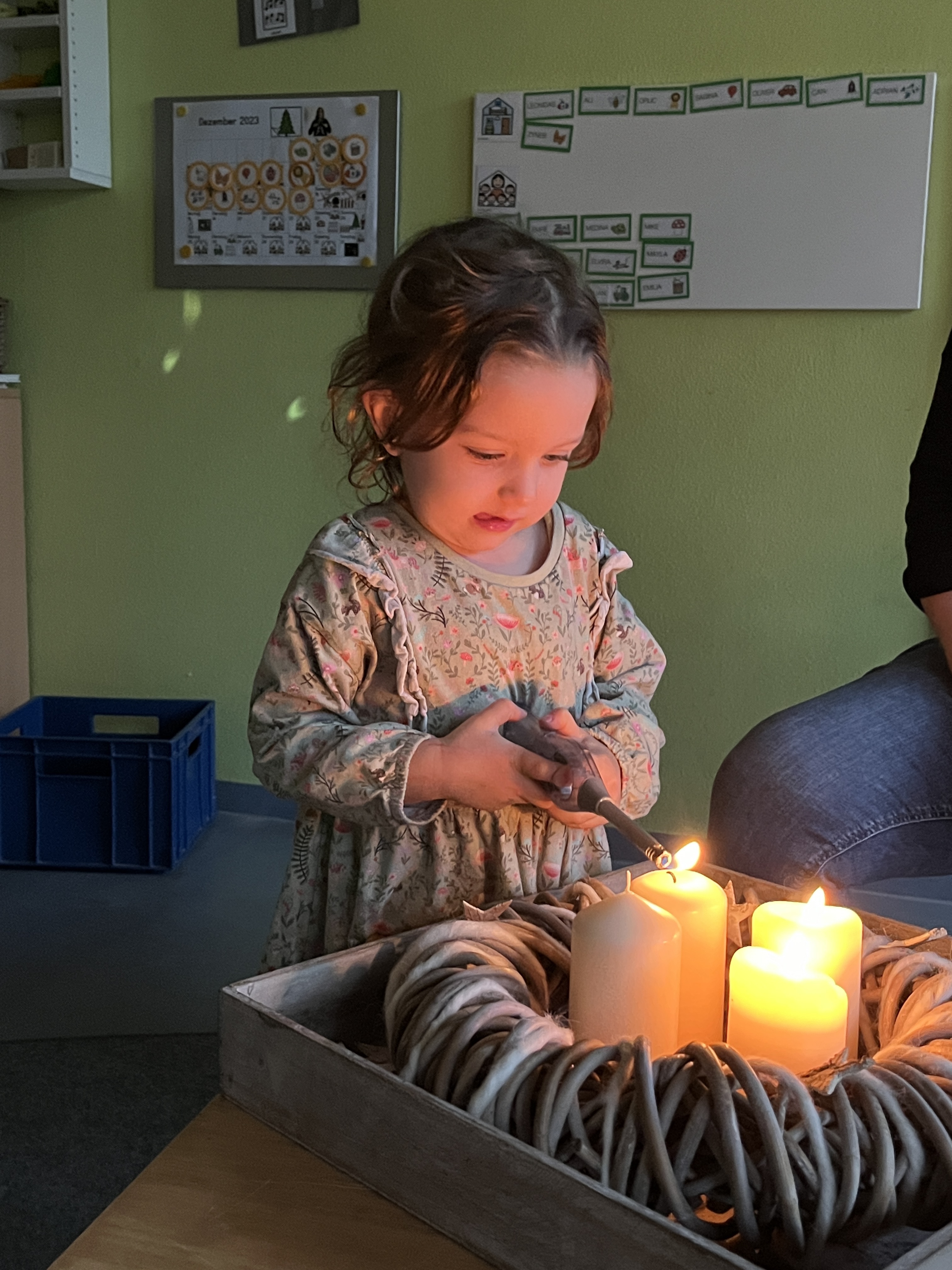 Ein Mädchen zündet die dritte Kerze am Adventskranz an.